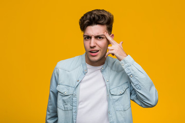 Young handsome student wearing a denim shirt showing a disappointment gesture with forefinger.