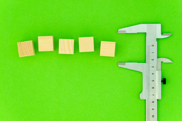 caliper holds empty wooden cubes. Place for your text. Green background, top view