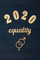 EQUALITY word carved out of plywood. Symbol of gender equality. Black wooden background. 2020