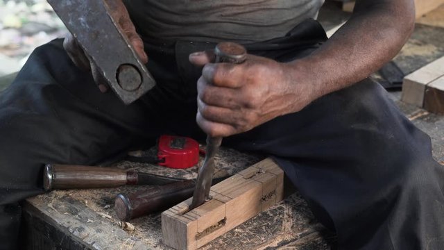 A carpenter making a hole in a wooden piece by hand using a hammer and a chisel