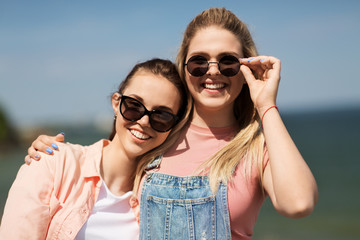 leisure and friendship concept - happy smiling teenage girls or best friends in sunglasses at seaside in summer