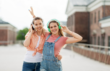 leisure, music and friendship concept - happy smiling teenage girls or best friends in headphones hugging on city street in summer