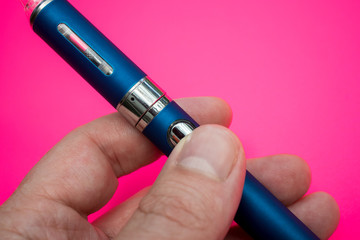 Hand holding vape pen metal electronic cigarette with vaping pink background