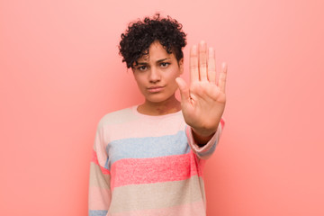 Young mixed african american teenager woman standing with outstretched hand showing stop sign, preventing you.