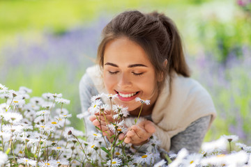 gardening and people concept - close up of happy young woman smelling chamomile flowers at summer...