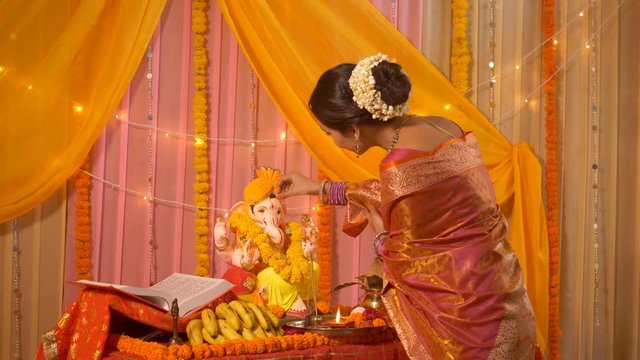 Indian woman dressed in traditional wear worshiping Lord Ganesha . Indian stock footage of a beautiful young woman dressed in ethnic wear and heavy jewelry for the festival of Ganesha Chaturthi