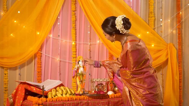 Indian woman applying tika to Lord Krishna's idol at home - Festival Celebration. 4k stock footage of Indian woman bowing head in front of Lord Krishna's idol at the temple at home