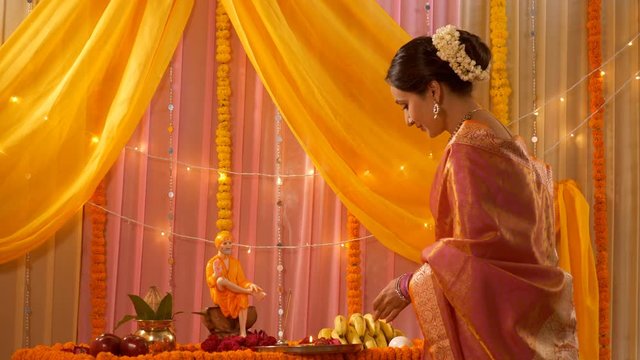 Young smiling Indian woman lighting up Diya for aarti during the festival - Guru Purnima. Indian stock video of a pretty lady in ethnic attire with folded hands and decorating puja thali for Sai Pu...