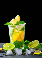 refreshing drink lemonade with lemons, mint leaves, ice cubes and lime in a glass on a black background, copy space