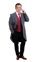 Full body portrait of handsome confident caucasian mature businessman 55-60 years old in grey tuxedo and red vest. Rich senior man talk by phone and looking to camera on isolated white background