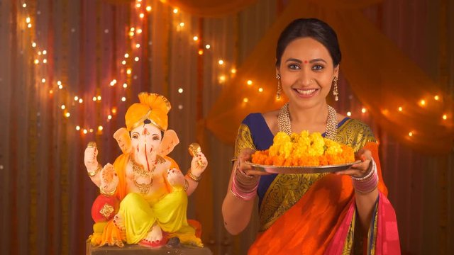 Beautiful Indian woman with flowers on pooja thali - celebrating Ganesh Chaturthi. Festival concept. Indian stock video of a middle-aged woman preparing for pooja wearing a saree