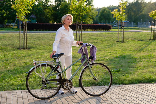 Full body Portrait of senior woman 60-65 years old on bicycle. Older lady riding city bike in european town. Old smiling female cycling with her bike in summer time.