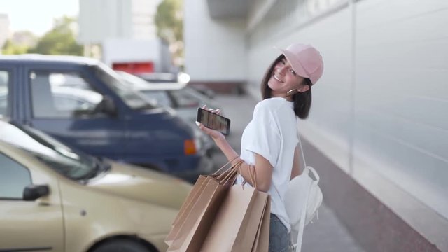 Stylish young woman posing with shopping bags outdoors, medium shot