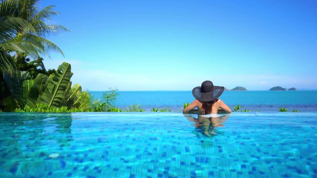 Woman in Infinity pool looks away at ocean on sunny day