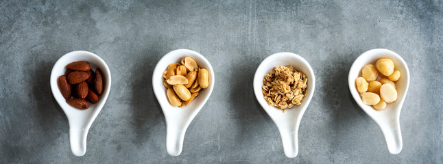 Healthy Foods. Mixed nuts in white bowls with nuts for diet on a concrete table. Different kinds of tasty and healthy nuts for text banner. Top view and copy space. Healthy Concept
