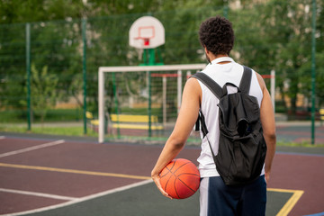 Rear view of young sportsman with black backpack and ball
