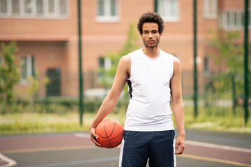 Young handsome basketball player with ball standing on the court