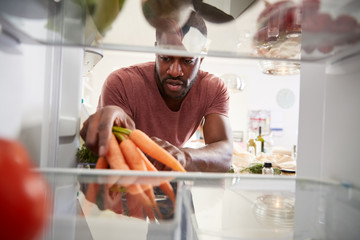 View Looking Out From Inside Of Refrigerator As Man Opens Door And Unpacks Shopping Bag Of Food