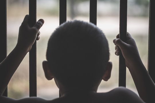 Hands of a young child clutching prison bars, victim child with locked in a cage cell, in emotional stress and pain, Children violence and abused concept.