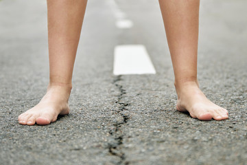 Bare feet of a young girl stand on the asphalt road close up.