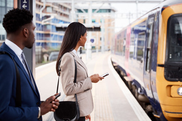 Businessman And Businesswoman Commuting To Work On Railway Platform Waiting For Train