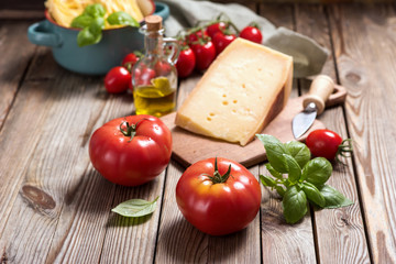 Cooking ingredients for italian cuisine, unsooked pasta, parmesan cheese, tomatoes, herbs on wooden background