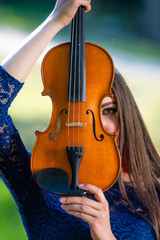 Portrait of a positive young woman. Part of the face is covered by the neck of the violin - image