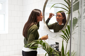 Businesswoman At Home Putting On Make Up In Mirror Before Leaving For Work