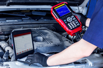 Closeup laptop screen with special software, equipment at vehicle with open hood. Repairman is conducting diagnostics and detecting problems at workshop. Mechanic is repairing car at service station.