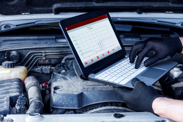 Mechanic is repairing car at service station. Closeup laptop screen with special software at...
