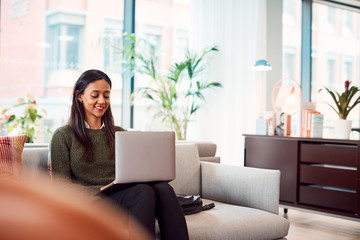 Businesswoman Sitting On Sofa Working On Laptop At Desk In Shared Workspace Office