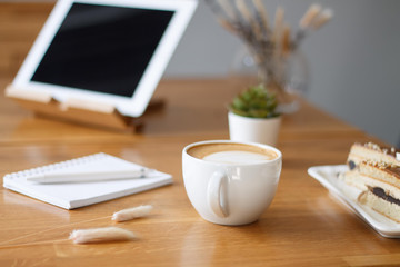 coffee in a Cup on a wooden table with a notebook and a tablet in the cafe work in the morning