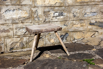 Old small wooden chair in the rural yard near a stone wall.