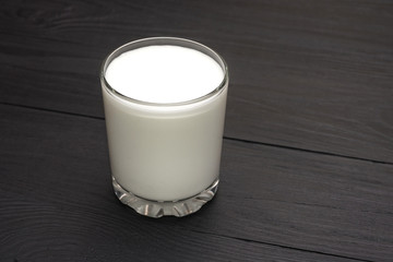 A glass with kefir, yogurt, milk on a black wooden background.