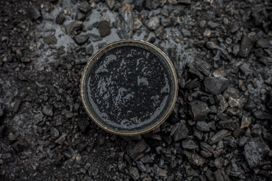 Close up of activated charcoal in a glass bowl on the wooden surface along with some raw powder of charcoal or coal spread on the surface.