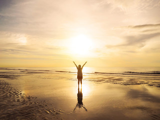 Back view Asian woman raised arms on air at sunset sea.