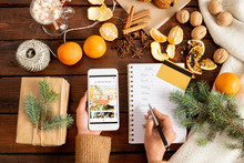 Female hands holding smartphone and making list of Christmas gifts