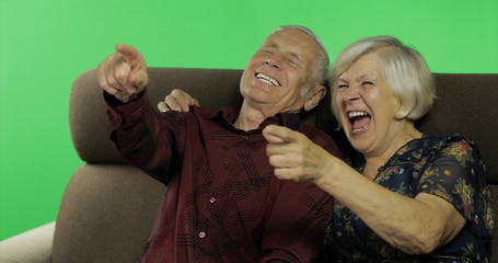 Senior aged man and woman sitting together on a sofa and watching TV. Chroma key