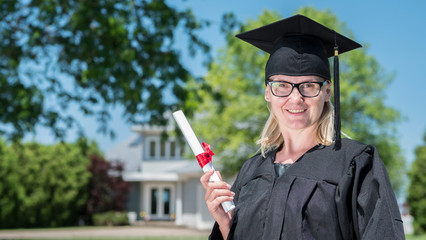 Portrait of a woman in a mantle and graduation cap, holding a diploma in her hand against the background of her house