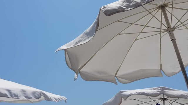 White sunshades parasols moving in the summer wind in front of the clear blue sky