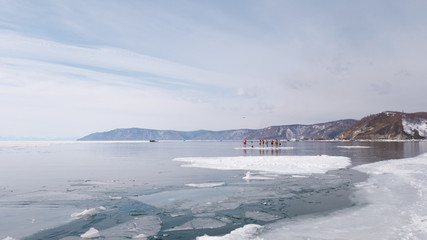 The source of the Angara river from lake Baikal. Spring day, people have fun on a floating ice floe in Siberia. Extreme people in Russia