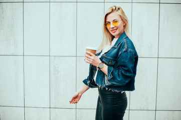 streetstyle fashion look, pretty cool smiling young woman with coffee cup walking in city, happy...
