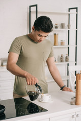 handsome asian man pouring coffee in cup from coffee pot in kitchen