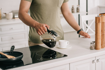 partial view of asian man pouring coffee in cup while standing near cooking surface in kitchen