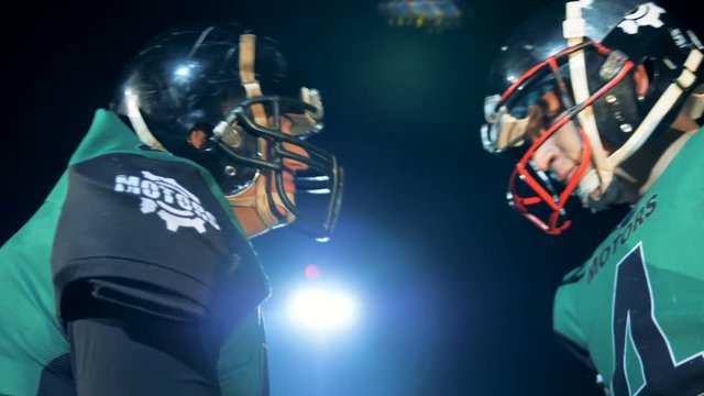 Two players shake hands and bump heads in helmets before a game on a field. 4K