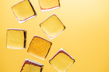 Stylish yellow background with transparent ice-like cubes for drinks. Flat lay macro photo.