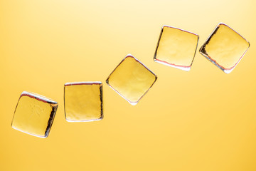 Stylish yellow background with transparent ice-like cubes for drinks. Flat lay macro photo.