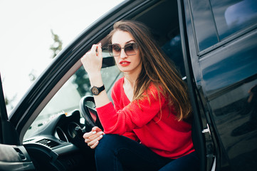 Fototapeta na wymiar Beautiful young woman in sunglasses and а watch on hand sitting in her black car and enjoy her life. fashion girl in automobile ready to travel! People Lifestyle Fashion Time concepts.