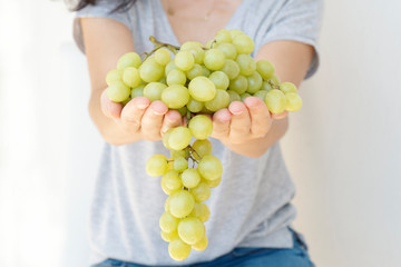 Beautiful woman, holding fresh green grape in hand, isolated on white background