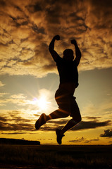 Silhouette of a young man in a jump against the backdrop of the setting sun and sky. The concept of happiness, activity, freedom, health. Man of dense build in a t-shirt and shorts. Place for text.